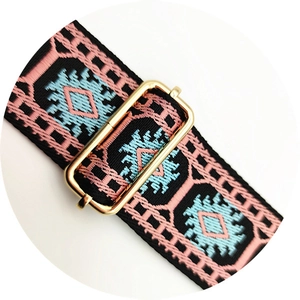 Close-up of ethnic style woven bag strap with pink geometric embroidery and gold buckle