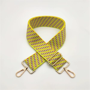 Close-up of yellow woven bag strap with red geometric pattern and gold metal hooks