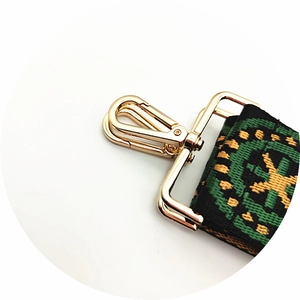 Detail of golden metal lobster clasp and ethnic green woven shoulder strap for bags