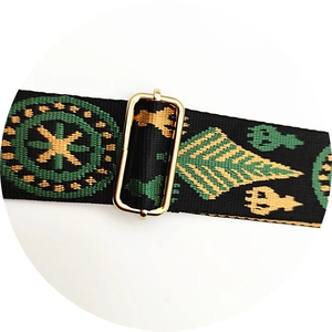Close-up of ethnic wide woven bag strap with green geometric patterns and gold metal buckle