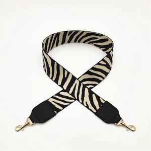 Macro detail of zebra pattern woven bag strap with golden lobster clasps and black leather ends