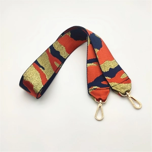 Detail eines breiten Jacquard-Taschengelenkriemens mit rot-gold-blauem Muster und Goldclips
