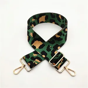 Detail of green leopard print wide bag strap with gold metal buckles and swivel hooks