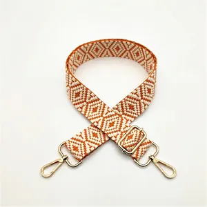 Detailed view of orange and white geometric woven bag strap with golden lobster clasps