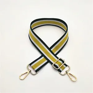 Close-up of yellow, white, and dark green striped nylon bag strap with gold metal hardware