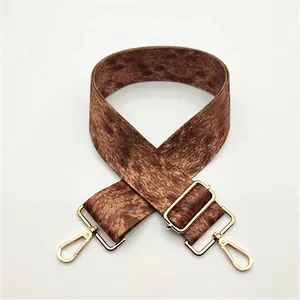 Detail of adjustable woven wide shoulder strap with brown pattern and gold metal hooks