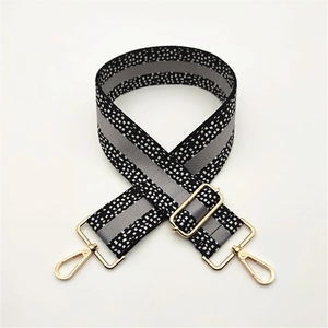 Detail of adjustable wide shoulder strap with black white pixel grid and gold metal buckle