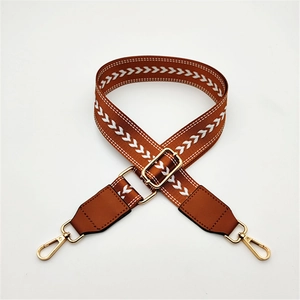 Detail of adjustable caramel brown woven strap with white V-pattern and gold hardware