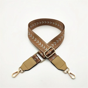 Close-up of adjustable brown bag strap with silver arrow pattern and golden metal buckles