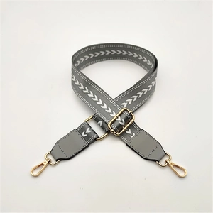 Macro detail of grey chevron woven shoulder strap with gold metal buckle and swivel hooks