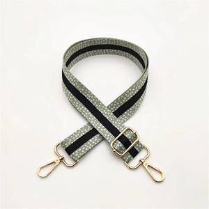 Détail d'une bandoulière tissée vert clair avec motif blanc et crochets dorés