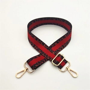 Close-up of adjustable leopard print bag strap with red stripe and gold metal buckles