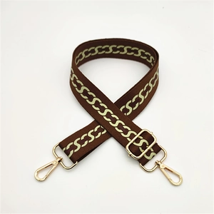 Detail of adjustable woven brown and yellow chain pattern bag strap with gold lobster clasps