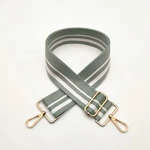 Detail of adjustable gray and white striped bag strap with gold metal hooks and buckle