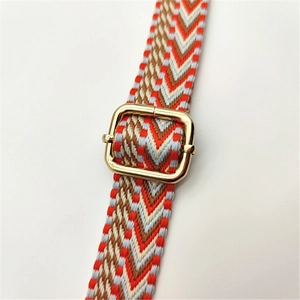Close-up of woven geometric bag strap in orange and brown with gold metal buckle