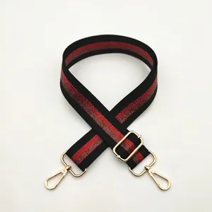 Detail view of adjustable woven bag strap with red stripes and gold hooks