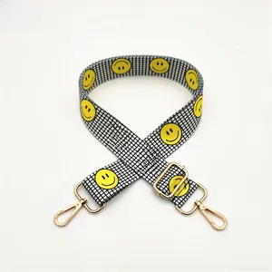 Detail of checkered woven bag strap featuring yellow smiley prints and gold metal hooks