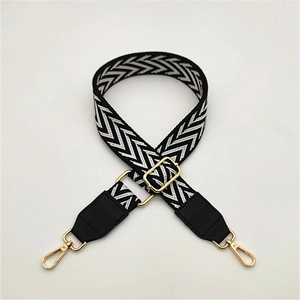 Close-up of adjustable woven black and white diamond pattern bag strap with gold lobster claw clasps