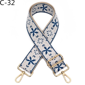 Detail of embroidered beige bag strap with blue floral patterns and gold metal clasps