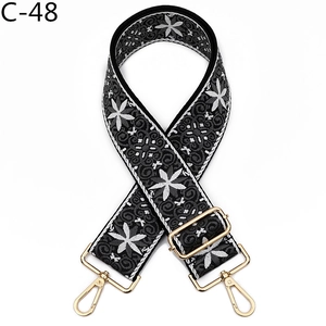 Close-up of wide embroidered bag strap with white flower patterns and gold buckles