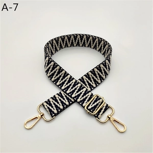 Macro detail of adjustable woven bag strap with black and white wave pattern and gold clasps