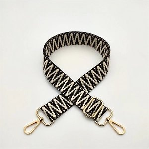 Detail of adjustable woven bag strap with black and white geometric pattern and gold buckles