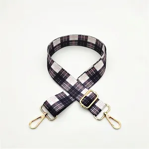 Detail of adjustable plaid bag strap with black, white, and pink weave and gold metal hooks