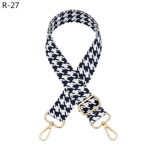 Detail of adjustable black and white houndstooth bag strap with shiny gold metal hooks