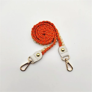 Close-up of woven orange and beige shoulder strap with gold metallic thread and lobster clasps