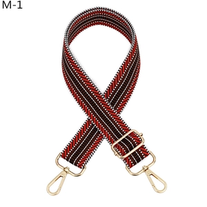 Détail d'une bandoulière en jacquard rouge et noir avec mousquetons dorés
