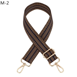Détail d'une sangle réglable à motif chevrons noir et marron avec mousquetons en métal doré