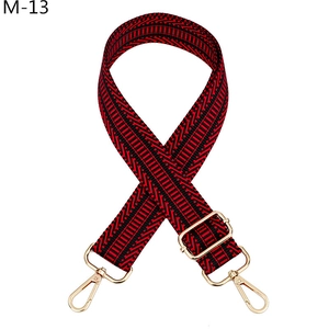 Détail de la bandoulière jacquard rouge et noire avec mousquetons et boucle dorés