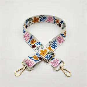 Détail d'une bandoulière blanche réglable avec imprimé floral et boucles dorées