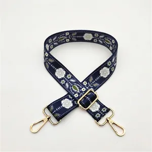 Détail d'une bandoulière brodée bleu marine avec crochets dorés et boucle de réglage en métal