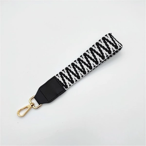 Detail of woven black and white geometric bag strap with leather ends and golden clasps