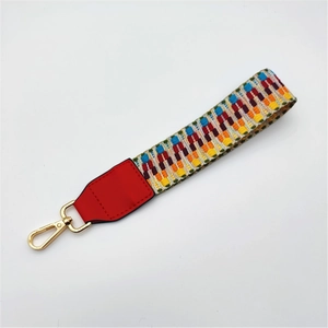 Detailed view of woven geometric bag strap with red leather end and golden lobster clasp