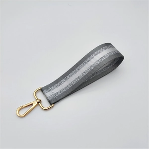 Close-up of gray woven wrist strap with silver reflective stripes and gold lobster clasp