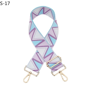 Close-up of wide woven bag strap with geometric patterns and gold metal buckles