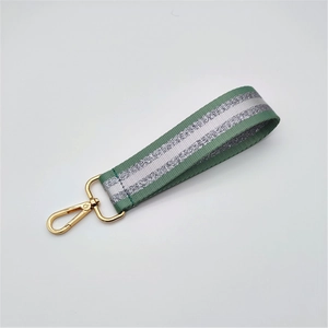 Close-up of green woven handbag strap with silver glitter stripe and gold lobster clasp
