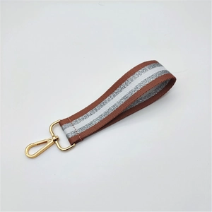 Close-up of woven wrist strap with brown and silver stripes and gold metal hardware