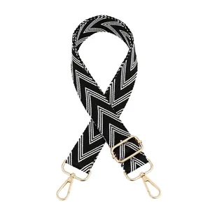 Detail of adjustable black and white herringbone patterned bag strap with gold metal hooks