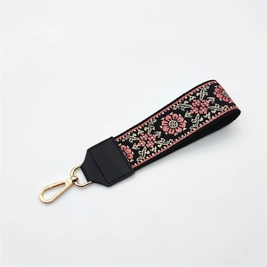 Detail of ethnic embroidery bag strap with pink floral patterns and gold metal lobster clasp
