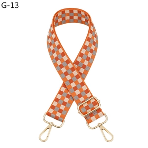 Detail view of woven plaid purse strap with orange and grey grid and gold metal clasps