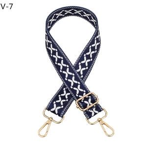 Detail of navy blue woven bag strap with white X pattern and gold metal buckles