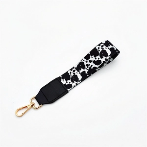 Close-up of cow print wrist strap with black leather detail and golden lobster clasp