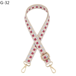 Macro detail of plaid woven bag strap with adjustable gold buckle and metal hooks