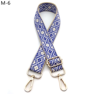 Detail eines verstellbaren blau-weißen Jacquard-Schultergurts mit goldenen Metallkarabinern