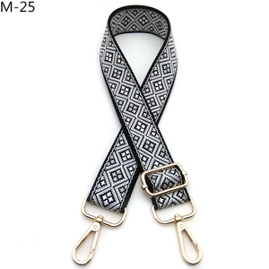 Detail eines schwarz-weißen Rauten-Jacquard-Taschenriemens mit goldfarbenen Metallhaken