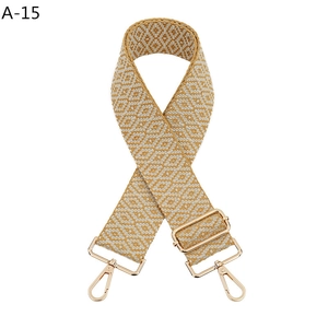 Nahaufnahme des geometrisch gewebten Gurts in Gelb und Beige mit goldfarbenen Karabinern