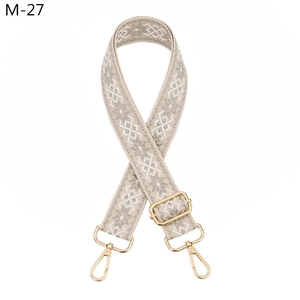 Close-up of beige geometric snowflake pattern adjustable bag strap with gold metal hooks